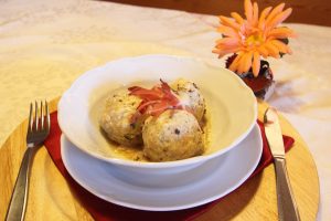 Un piatto con all'interno tre canederli e, accanto, un fiore