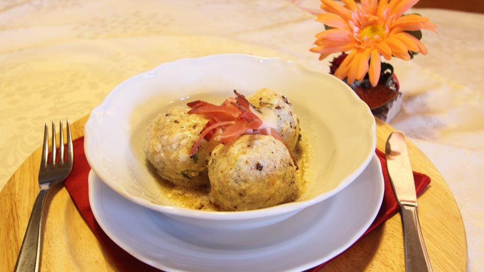 Un piatto con all'interno tre canederli e, accanto, un fiore