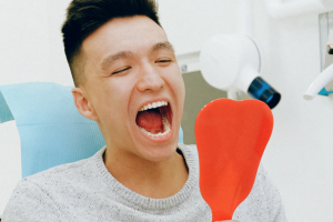 Un ragazzo, seduto su una poltrona di un dentista, si guarda la bocca con uno specchio dopo un trattamento