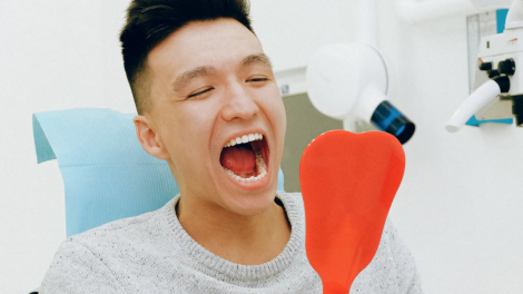 Un ragazzo, seduto su una poltrona di un dentista, si guarda la bocca con uno specchio dopo un trattamento