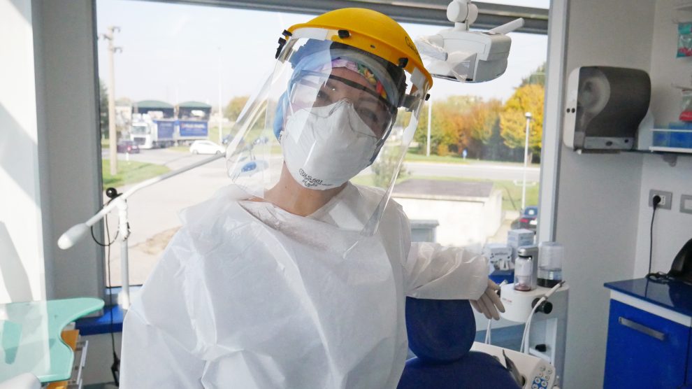 Una igienista dentale di Amicodentista sorride sotto tutti i dispositivi di protezione individuale necessari per la prevenzione della diffusione del covid 19: visiera, mascherine, camici, guanti etc