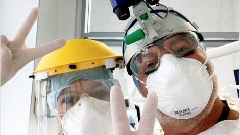 Un dentista e la sua assistente salutano in camera facendo il gesto della vittoria, completamente bardati con i dispositivi di protezione individuali richiesti dalle misure di prevenzione contro la diffusione del covid19