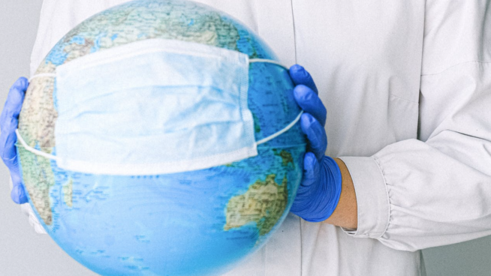 Un dottore tiene un mappamondo tra le mani e gli fa "indossare" una mascherina chirurgica