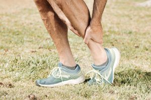 Un uomo sportivo, inquadrato dal ginocchio in giù, si tiene con entrambi le mani la caviglia sinistra