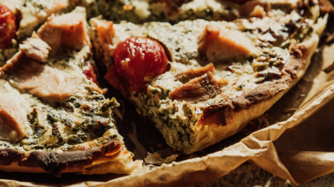 Una foto di una torta salata a base di spinaci e formaggio, decorata con alcuni pomodorini