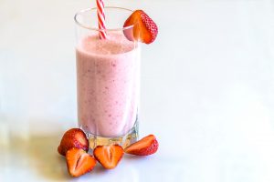 Un frullato / milkshake di fragole e banana all'interno di un bicchiere con cannuccia e fragole