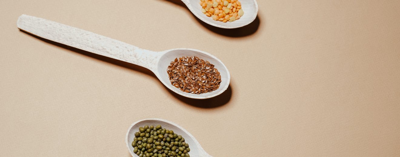 Tre mestoli di legno che contengono legumi, tra cui piselli e lenticchie