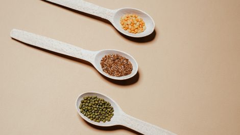 Tre mestoli di legno che contengono legumi, tra cui piselli e lenticchie