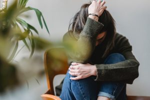 Una ragazza è accovacciata su una sedia in legno, si tiene con un braccio le ginocchia e con l'altro la testa.