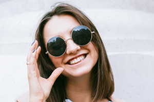 Una ragazza sorride mentre indossa un paio di occhiali da sole scuri con lenti tonde e molto grandi