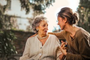 Una donna anziana seduta a fianco di una donna giovane: sorridono mentre parlano tra loro